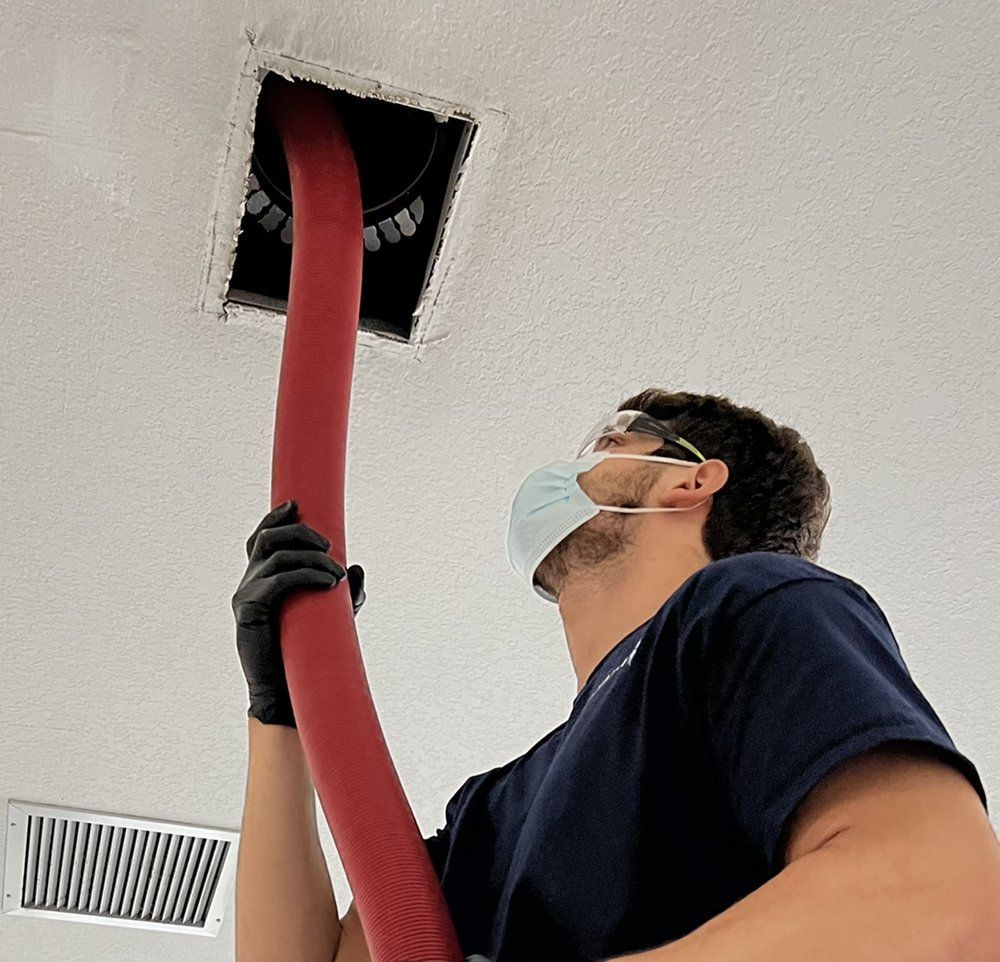 A man wearing a mask is using a red hose to clean a vent