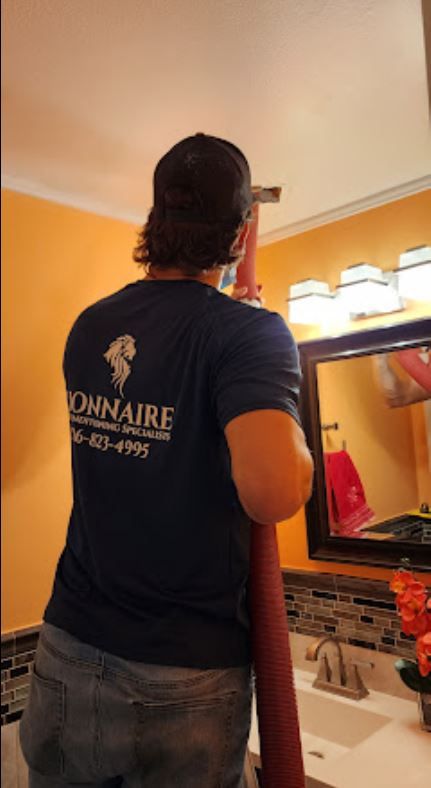 A man in a blue shirt is standing in front of a bathroom mirror.