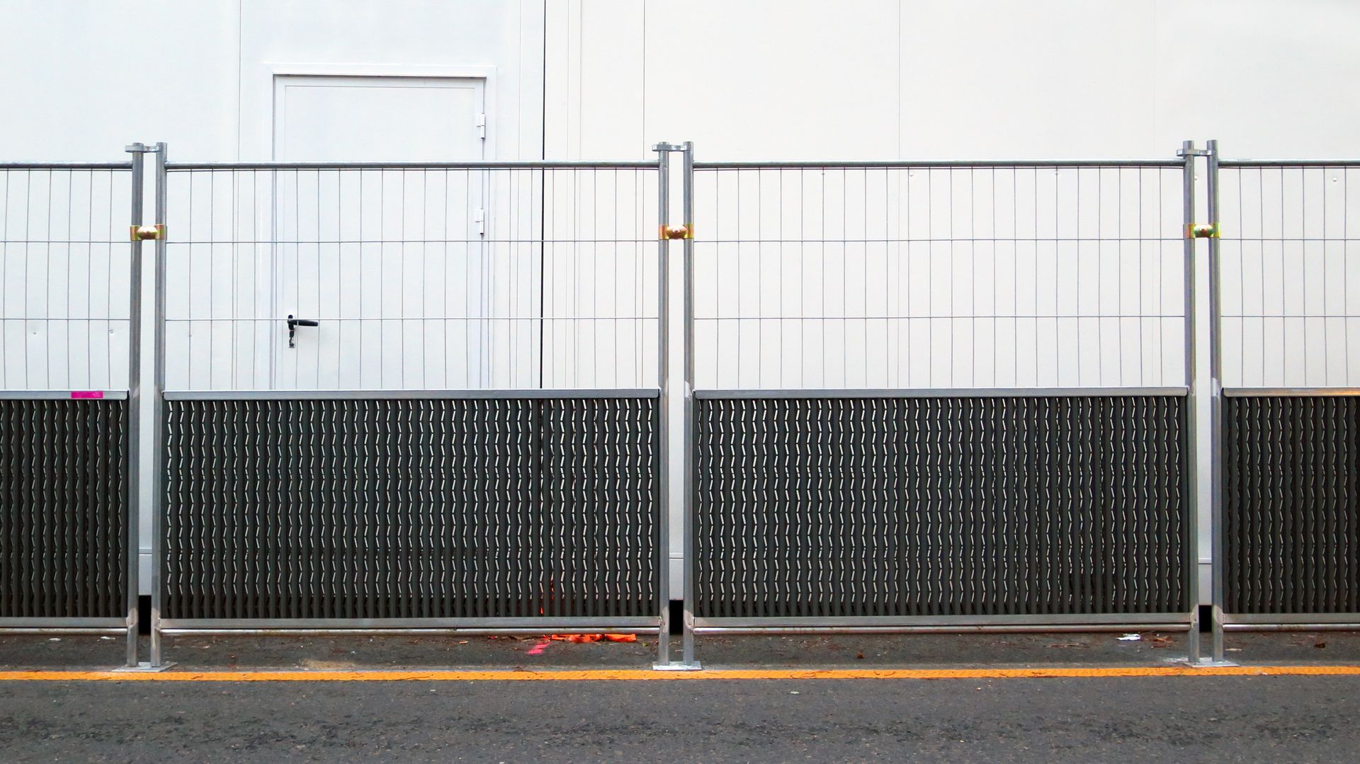 A metal security fence placed along a sidewalk in front of a white building wall with a closed door