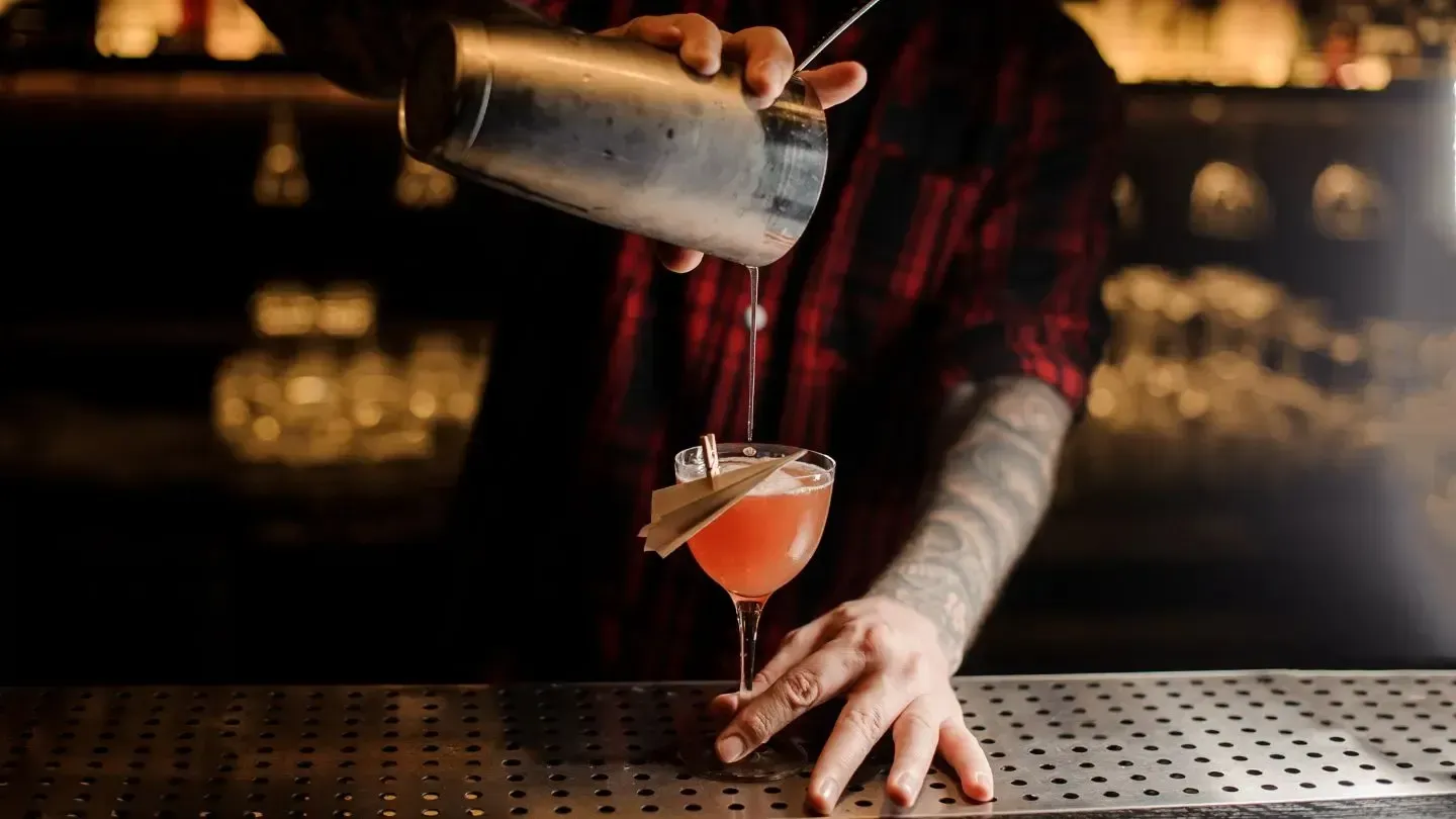 A bartender is pouring a cocktail into a martini glass.