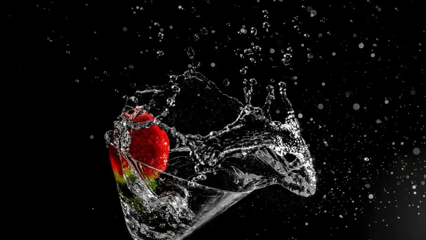 A strawberry is splashing into a glass of water on a black background.