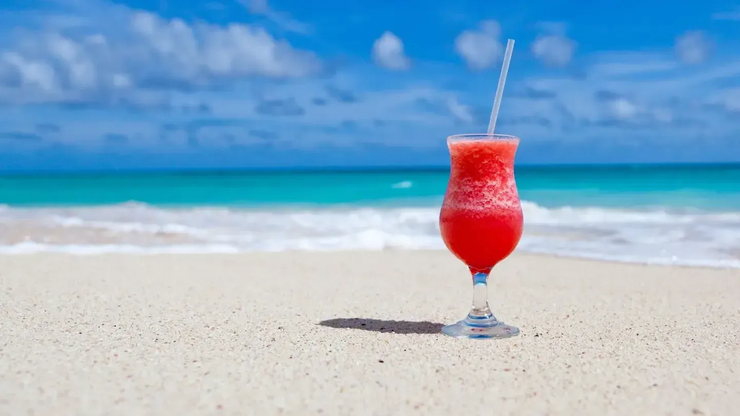 A red cocktail with a straw in it is on the beach.