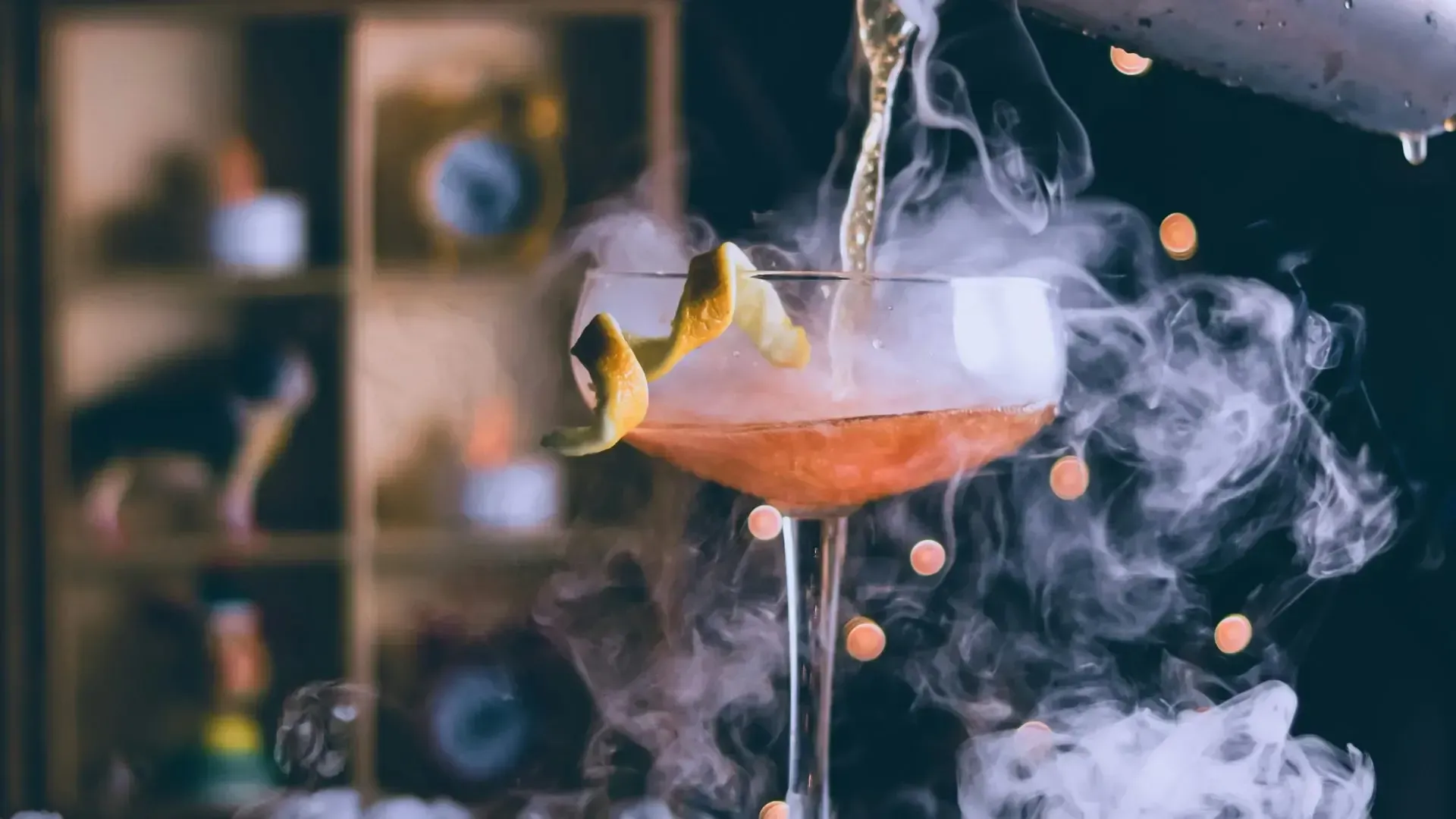 A cocktail is being poured into a martini glass with smoke coming out of it.