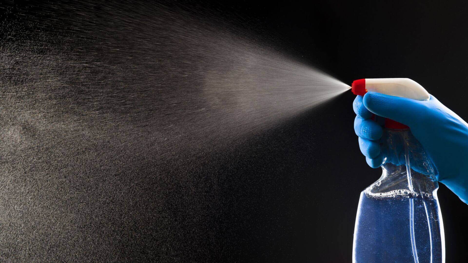 A person is spraying a bottle of cleaner on a black background.