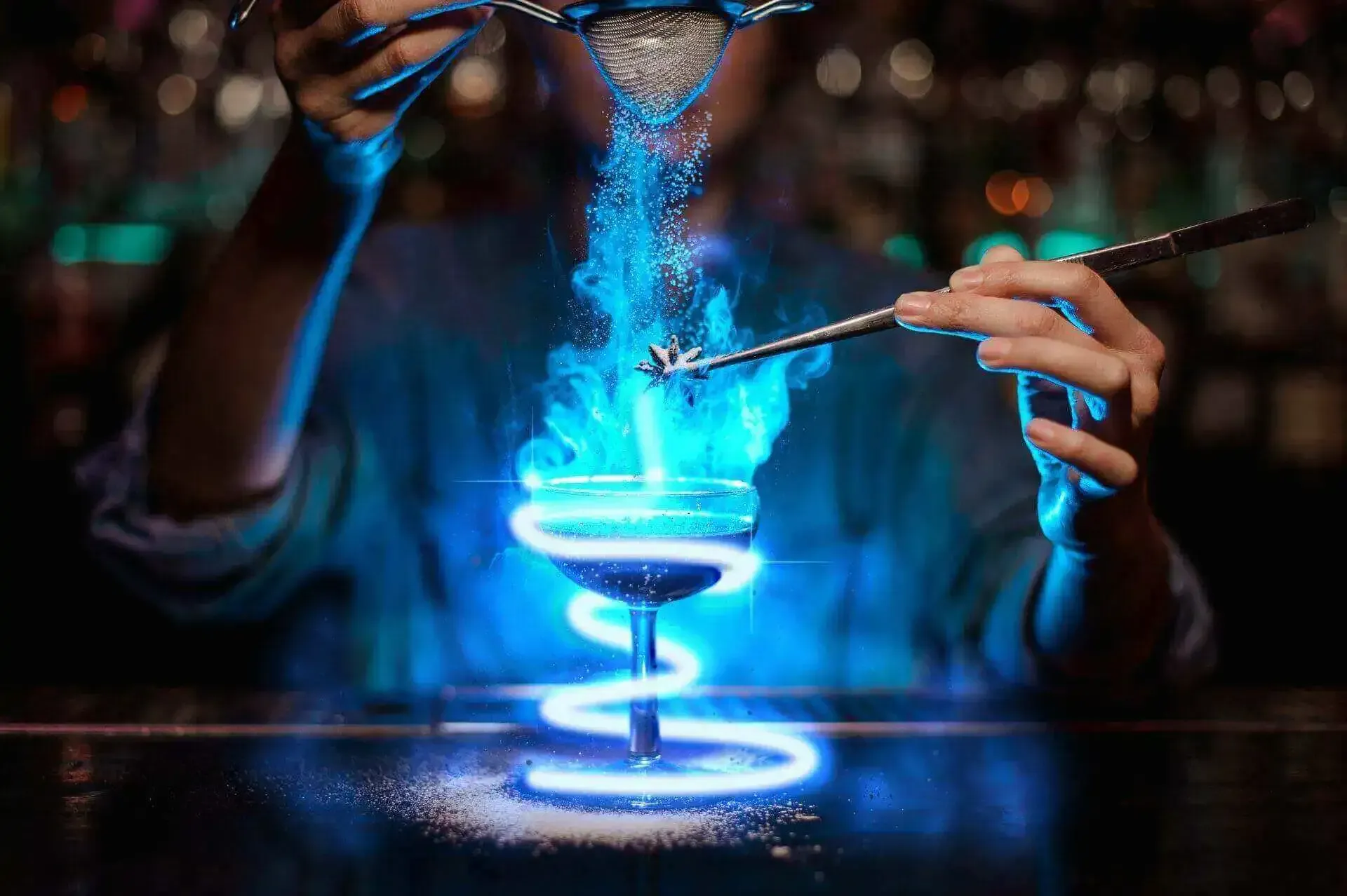 A bartender is pouring a drink into a glass with blue flames coming out of it.