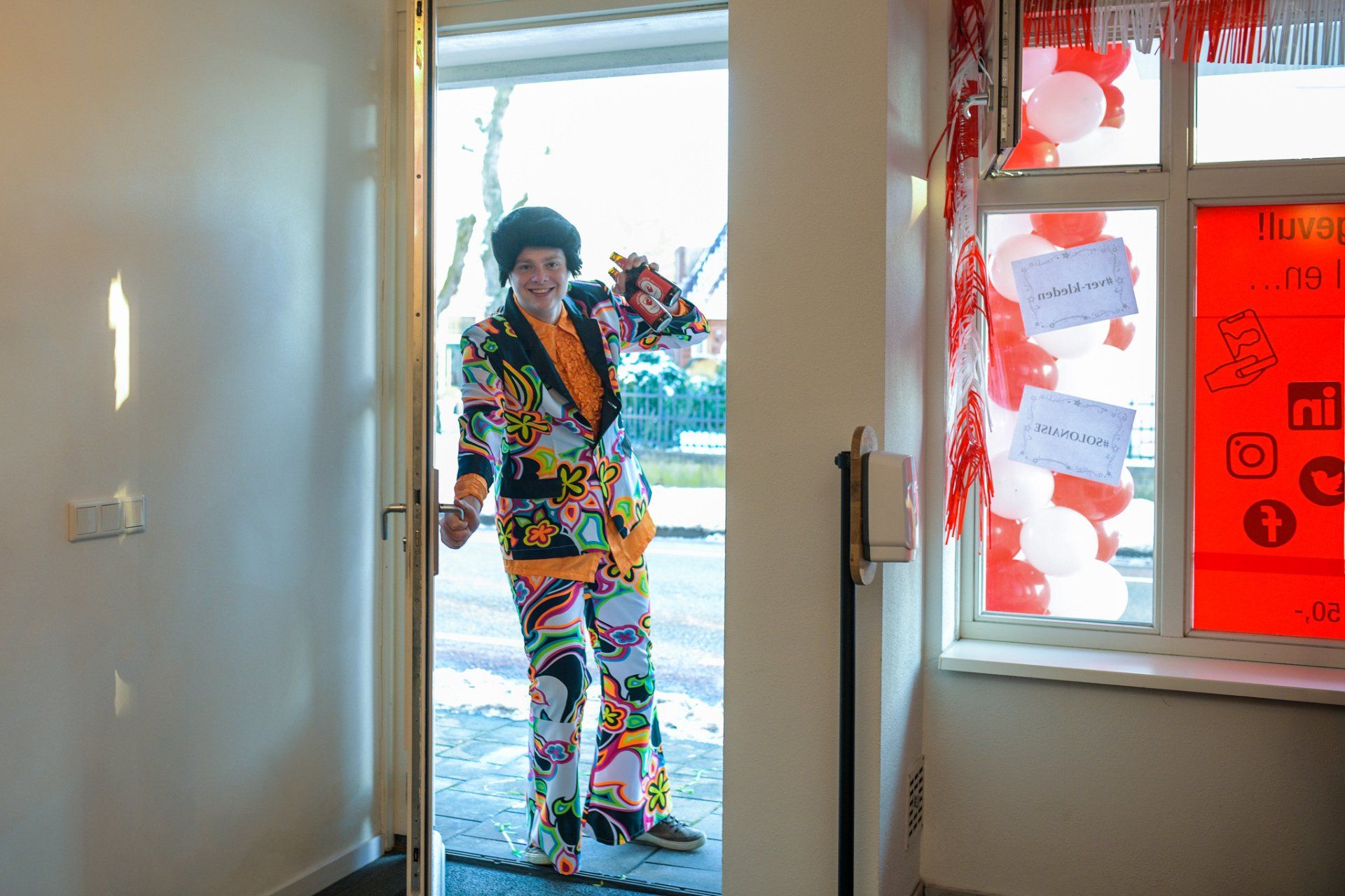 Een man in een kleurrijk pak staat in een deuropening.