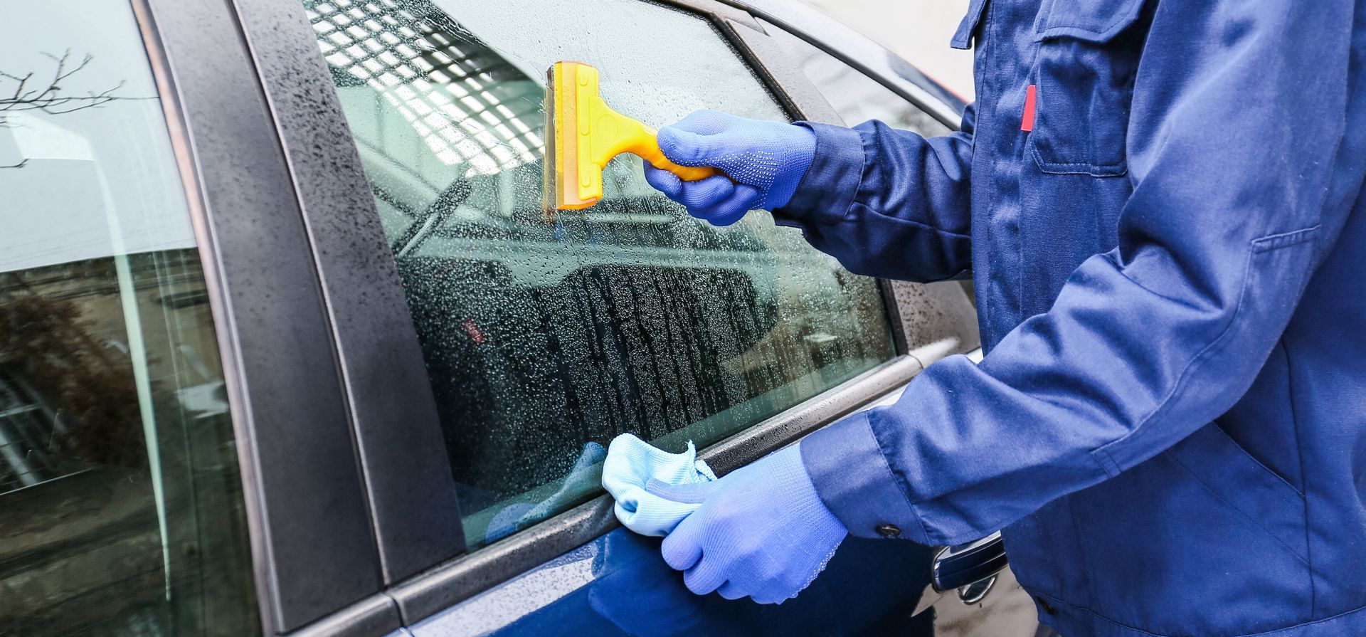 Person in blue gloves cleaning a car window with a yellow squeegee and a cloth. Person in blue gloves cleaning a car window with a yellow squeegee and a cloth.