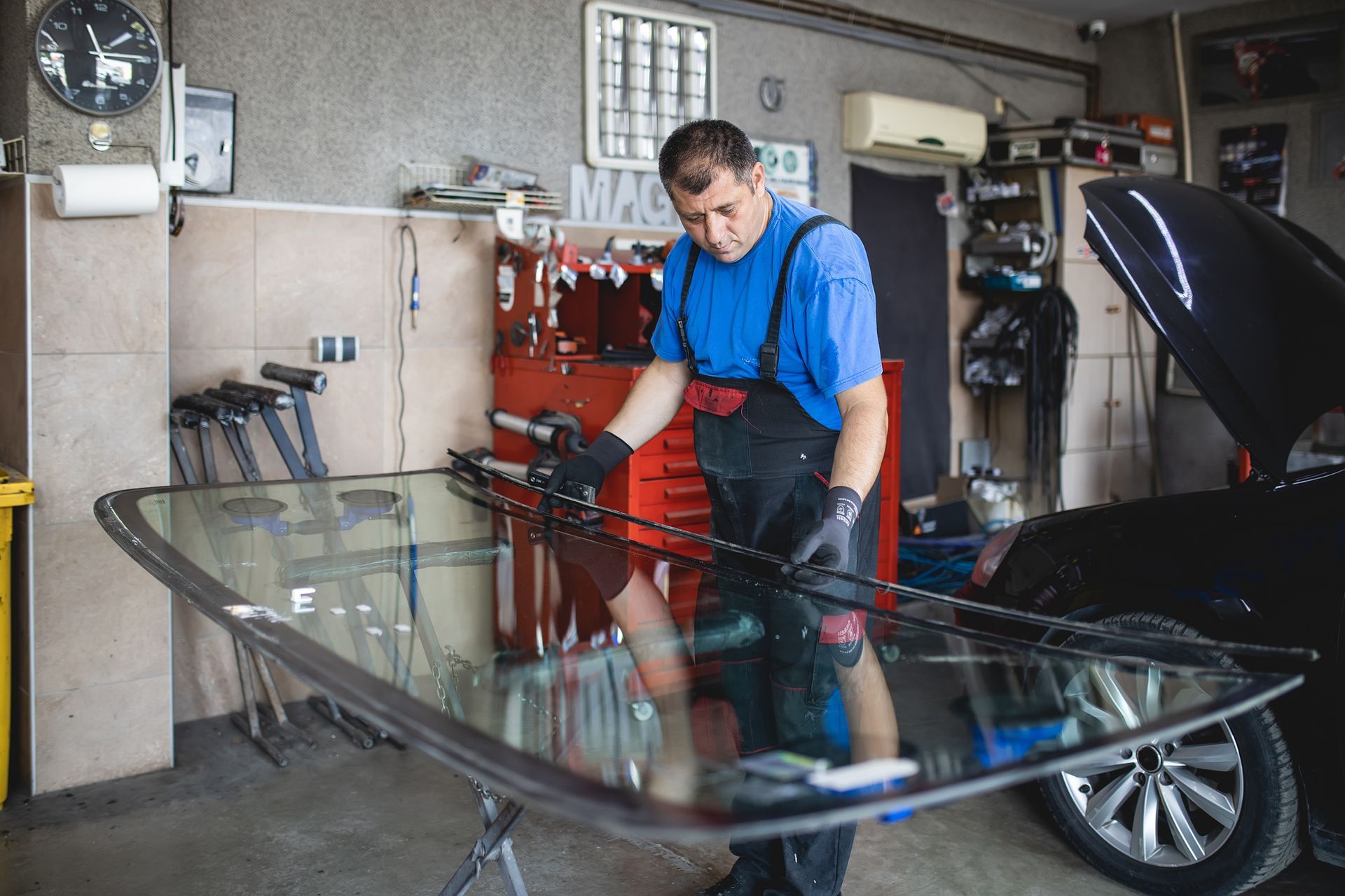 Mechanic in blue overalls installing windshield in a garage. Mechanic in blue overalls installing windshield in a garage.