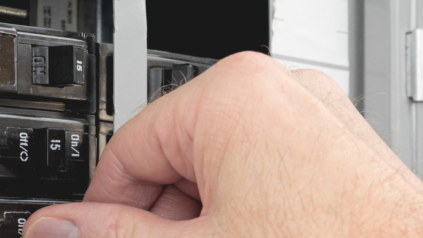 Hand flipping a circuit breaker switch in a black electrical panel.