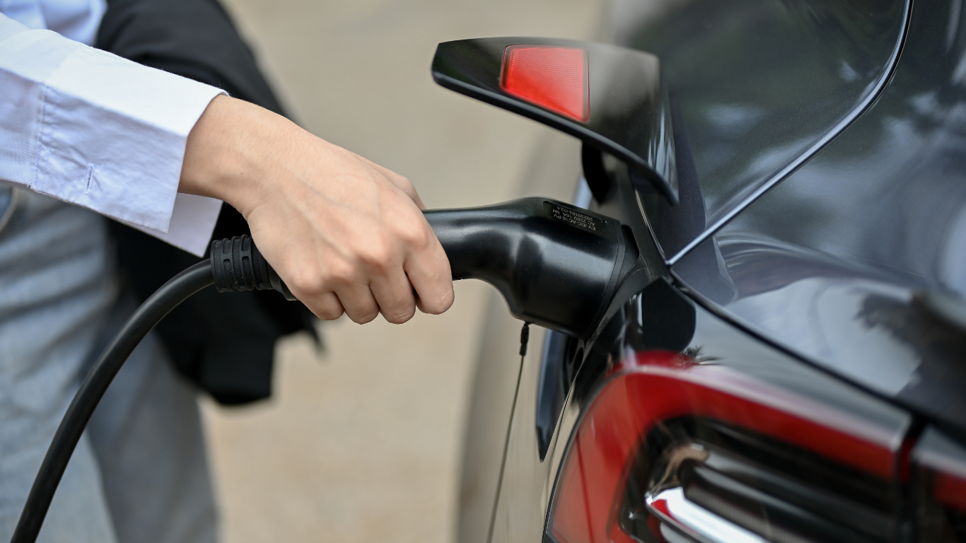 Person plugging an electric vehicle with a black charging cable.