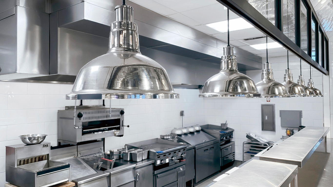 Commercial kitchen with stainless steel equipment and hanging pendant lights.