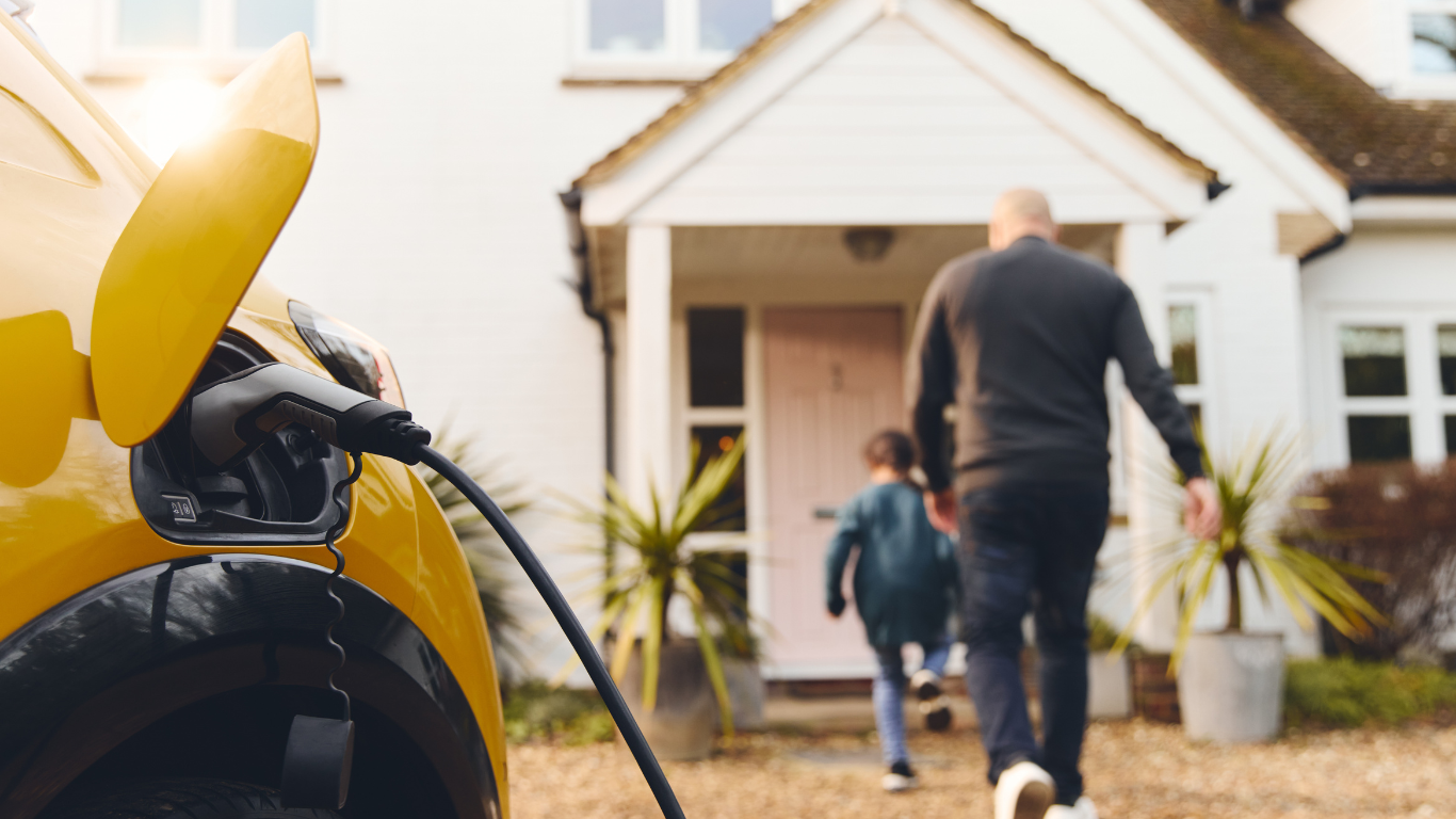 Yellow electric car charging, family walking toward a home's front door.