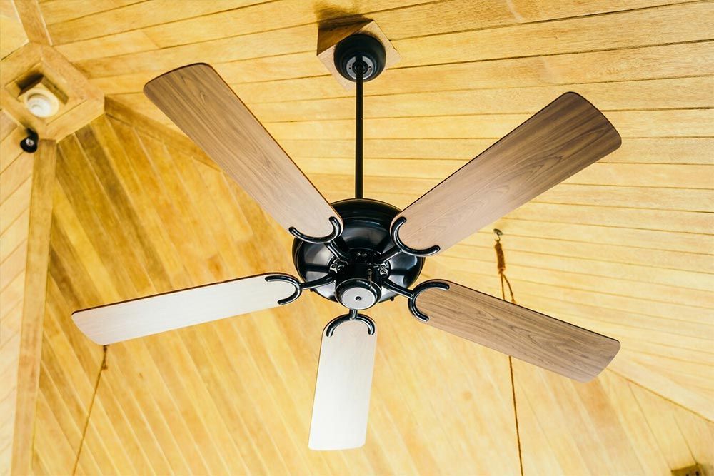 Ceiling fan with wooden blades, hanging from a wood-paneled ceiling.