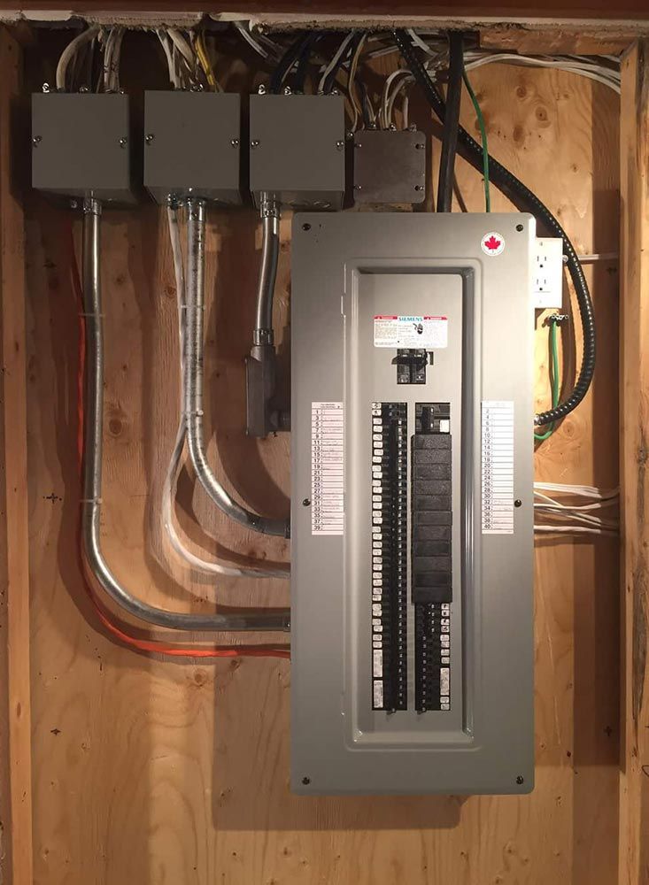 Electrical panel with multiple conduit lines and junction boxes mounted on a wooden wall.