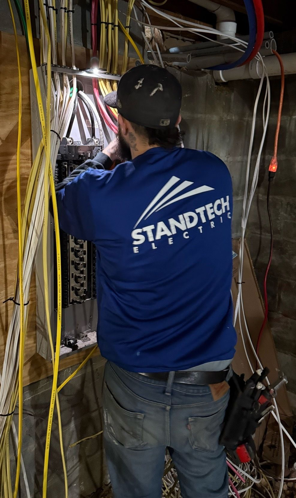 Electrician in a hard hat tests electrical panel with a multimeter.