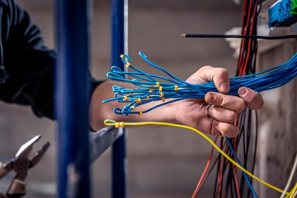 Hand holding blue electrical wires, with tools and wires in a cluttered indoor setting.