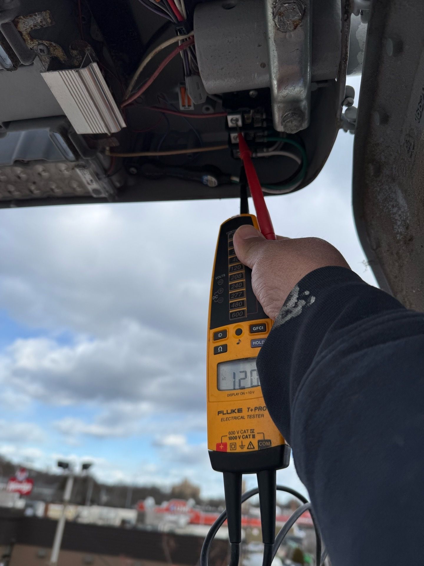 Man in red shirt installing a ceiling fan in a room with a white ceiling.