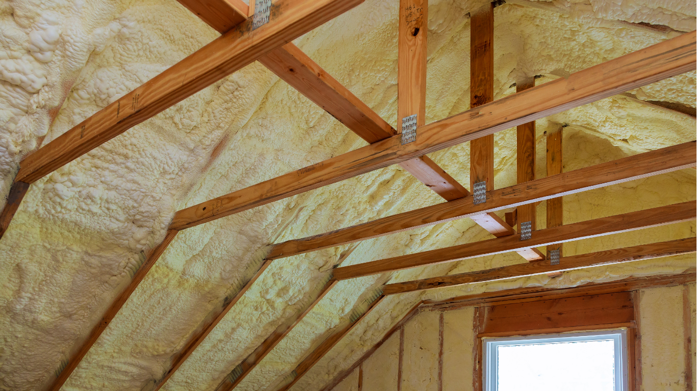 Attic roof rafters and interior walls insulated with sprayed yellow foam in an unfinished wooden framing structure.