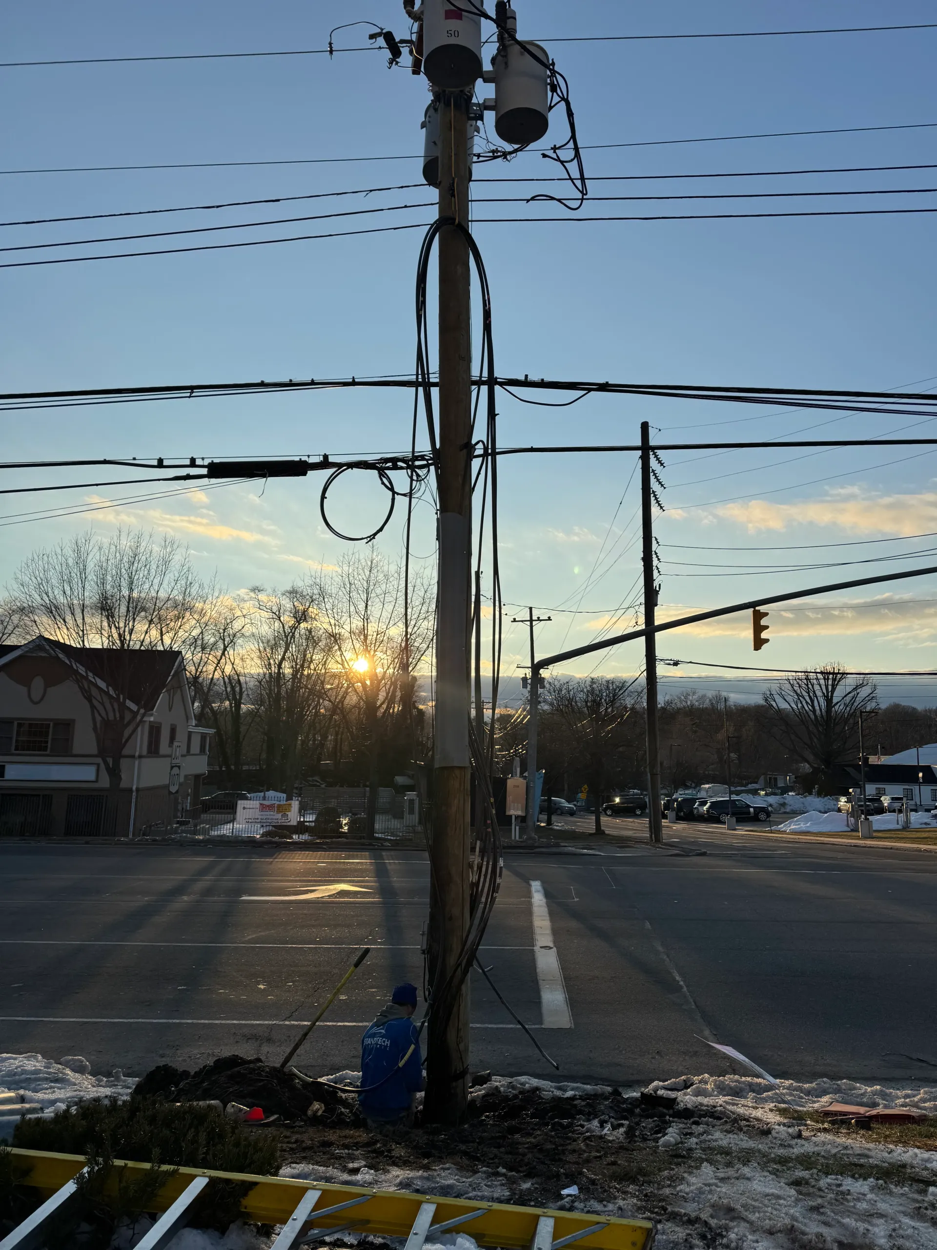 Man in a brown hoodie and cap installing a ceiling fan in a room.
