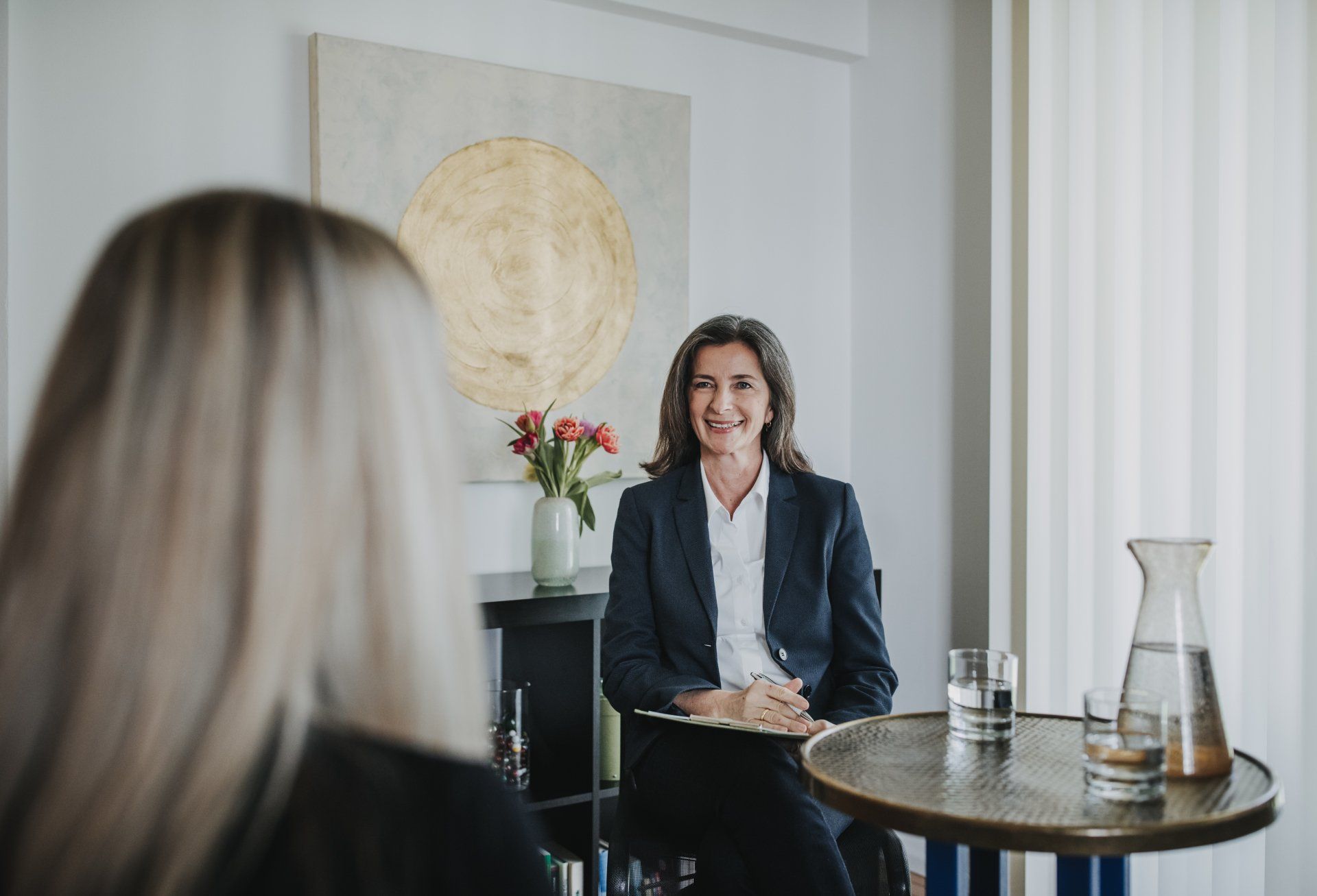 Eine Frau sitzt an einem Tisch und unterhält sich mit einer anderen Frau.