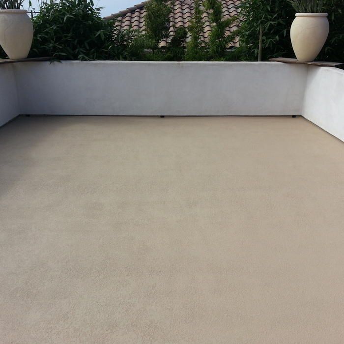 Tan rooftop terrace with white walls, two urns, and green foliage in the background.
