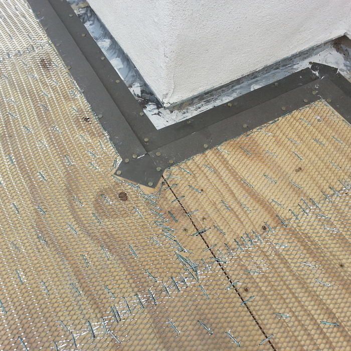 Gray metal flashing, a corner of a white wall, and wooden floor with a mesh covering.