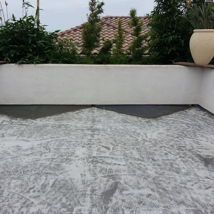 A rooftop patio with a white wall and plants in the background, gray painted floor, and a large pot.