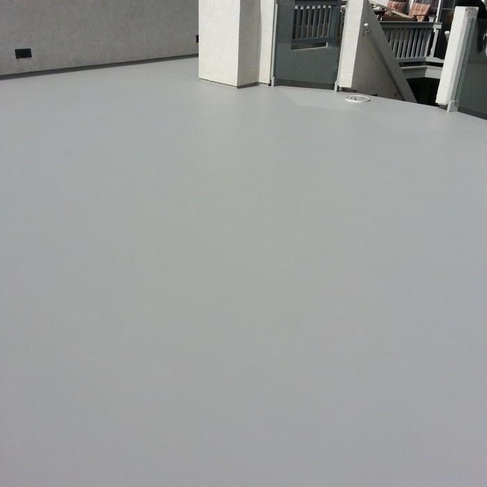 Gray painted rooftop with white pillars, railings, and a wall visible in sunlight.