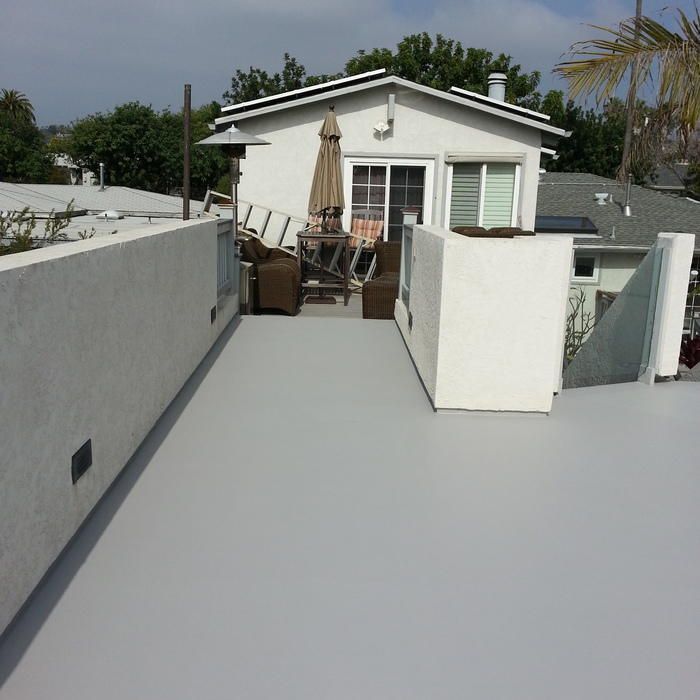 Gray rooftop patio with white walls, outdoor furniture, and a house in the background.
