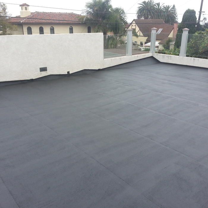 A flat roof covered in dark gray material, with white walls and a view of buildings in the background.