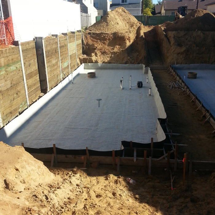 Construction site with excavated foundation, soil walls, concrete slab, wooden framework.