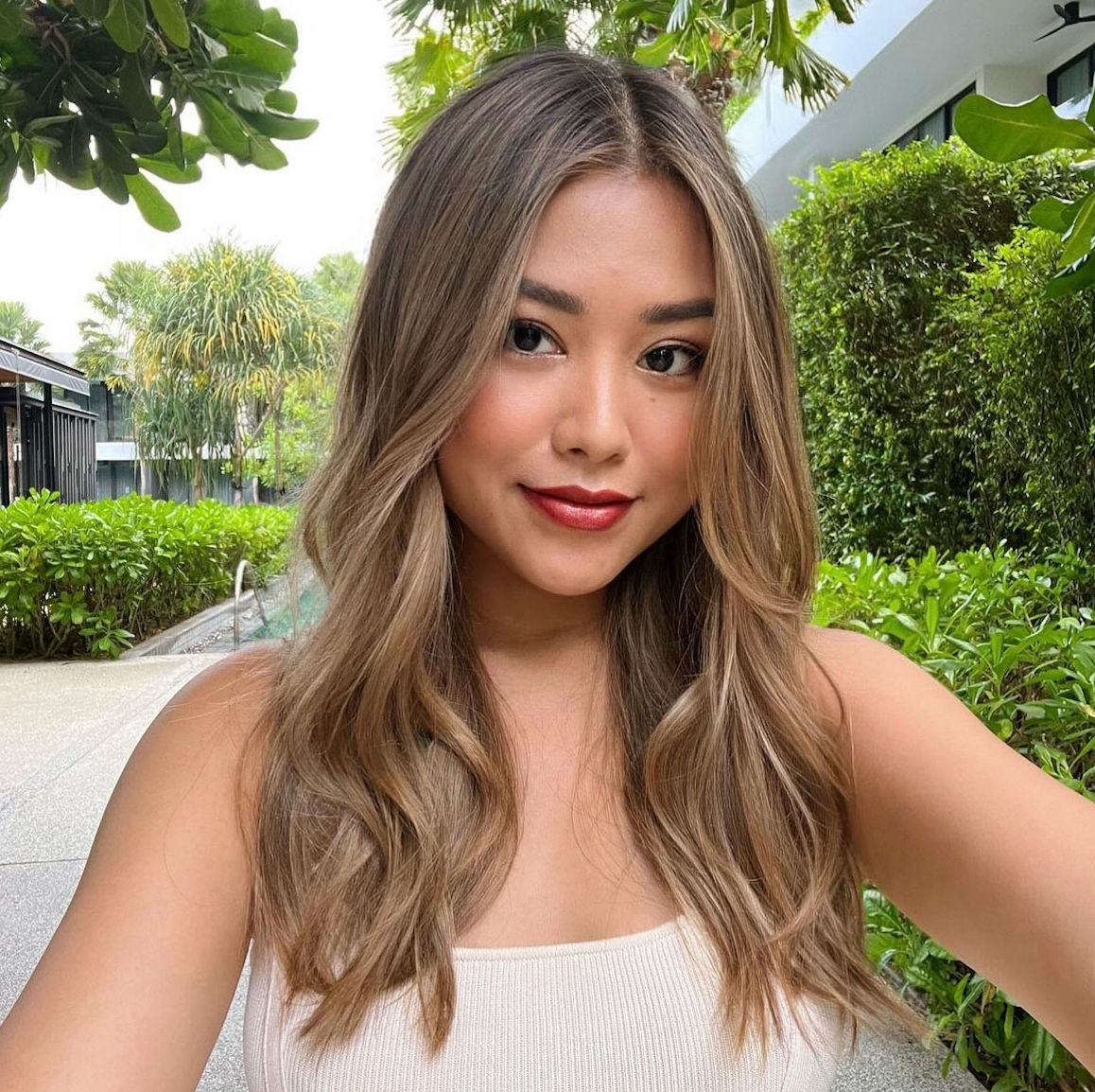 A woman in a white tank top is taking a selfie.
