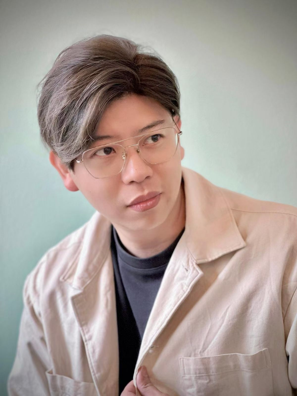 Man wearing glasses and a tan jacket, looking slightly off-camera with a neutral expression.