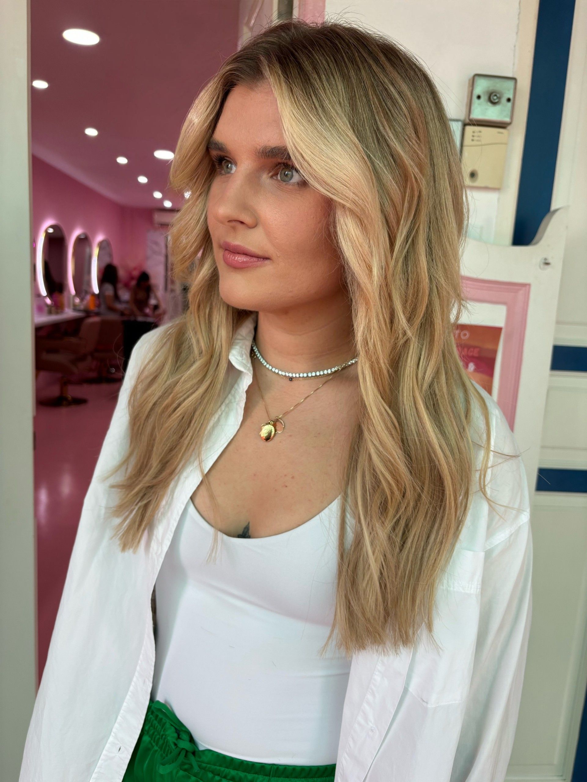 A woman with long blonde hair is wearing a white shirt and green shorts.