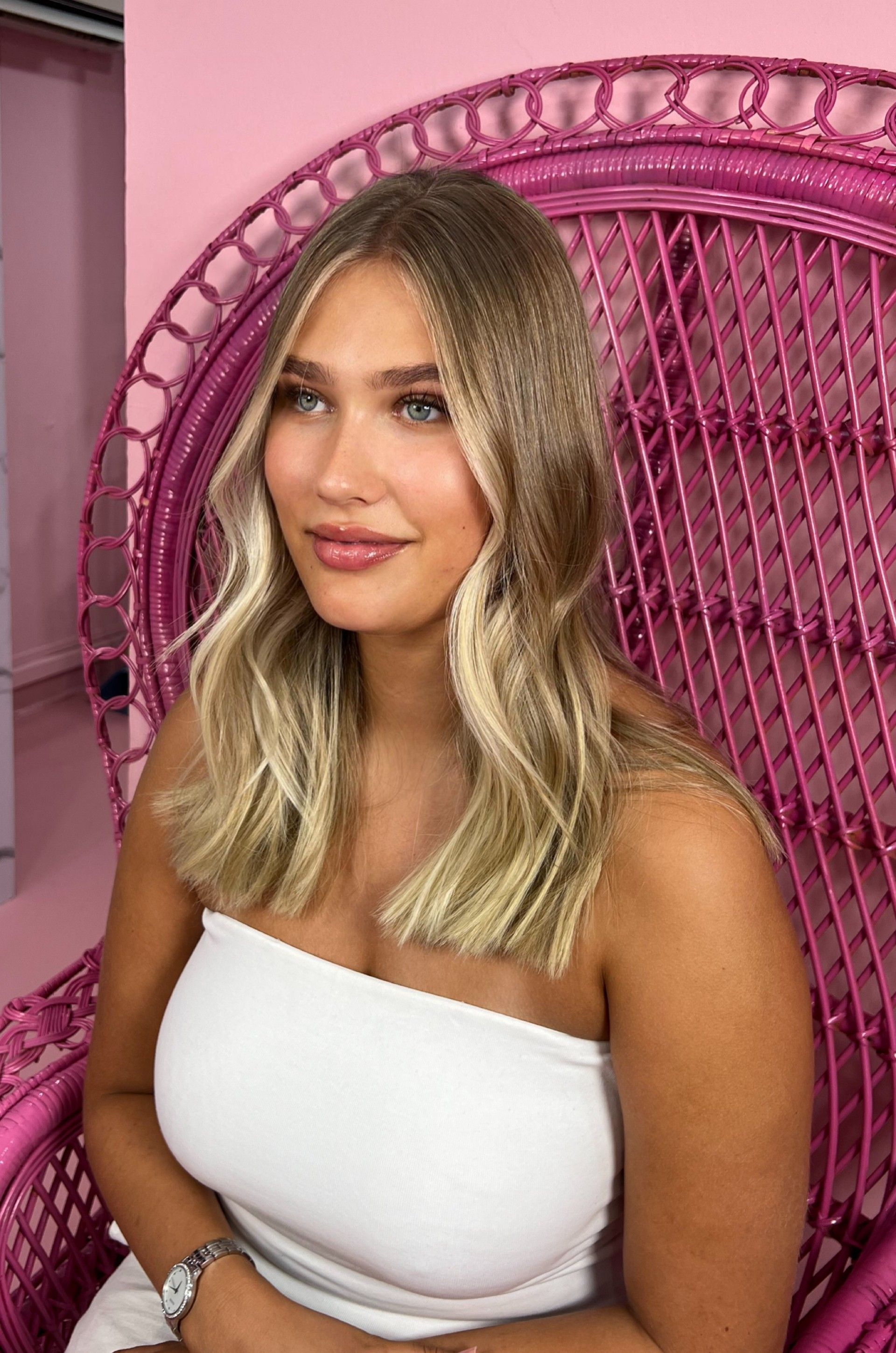 A woman in a white top is sitting in a pink chair.