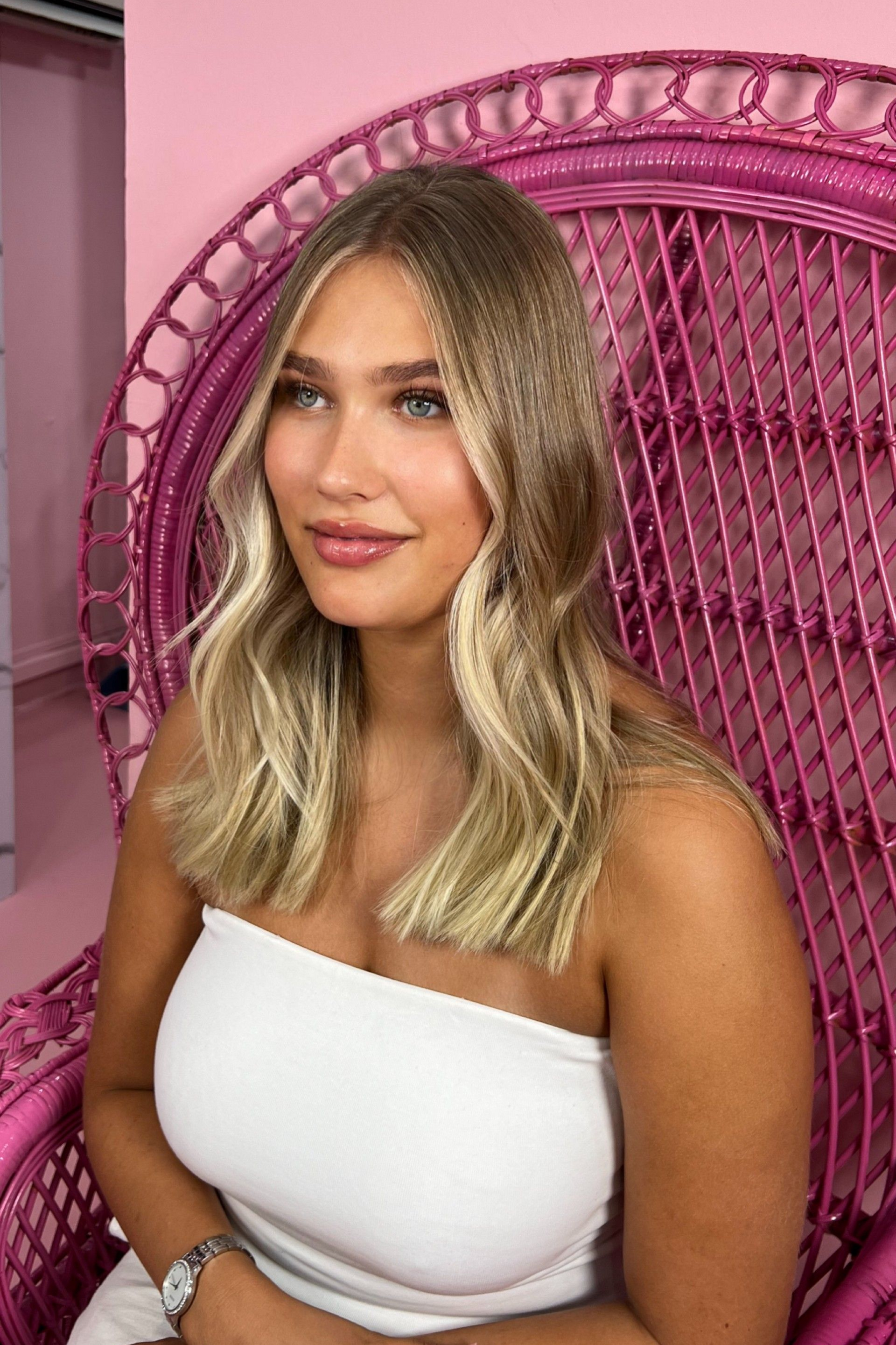A woman in a white top is sitting in a pink chair.