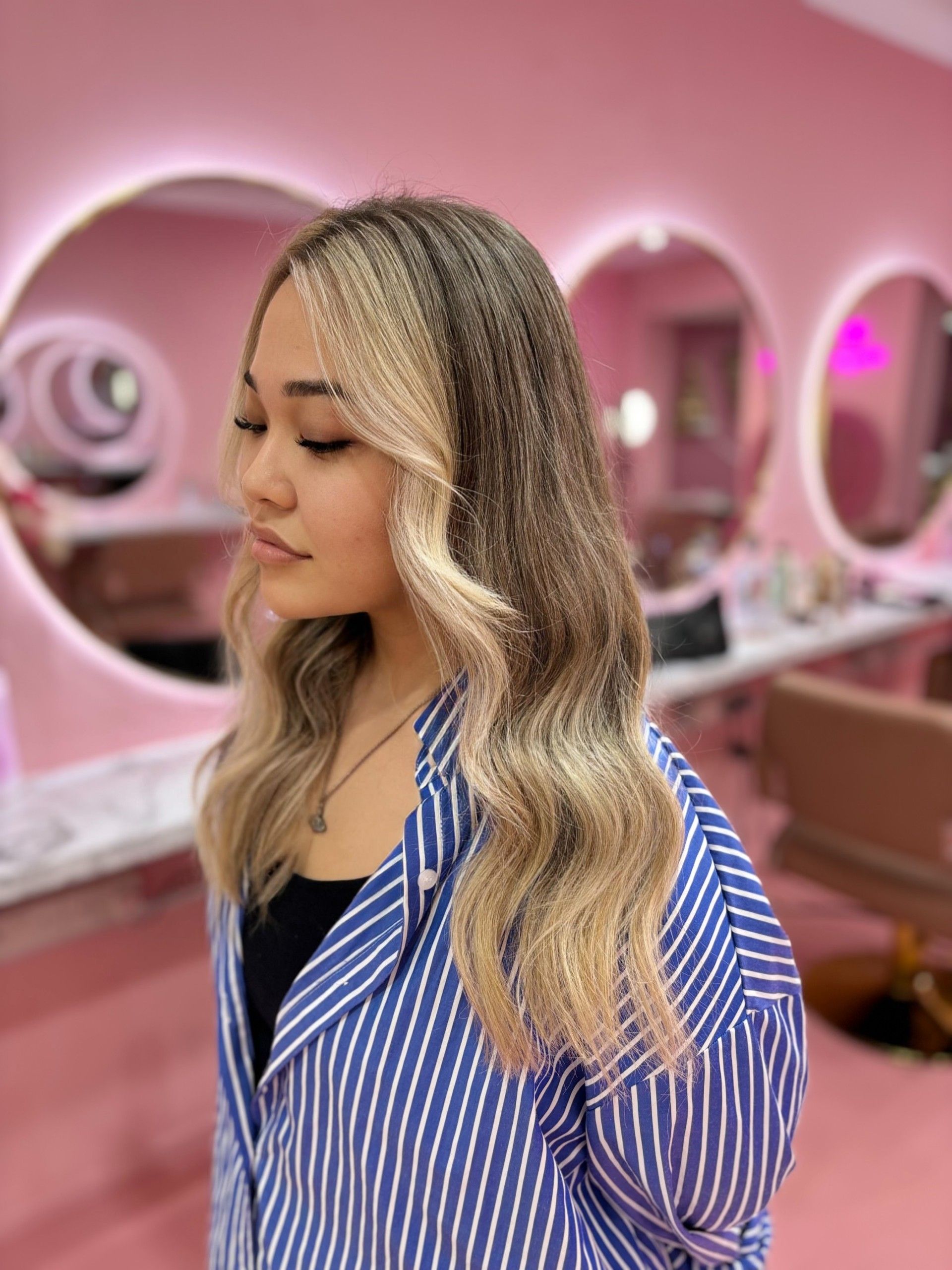 A woman in a blue and white striped shirt is standing in a pink room.