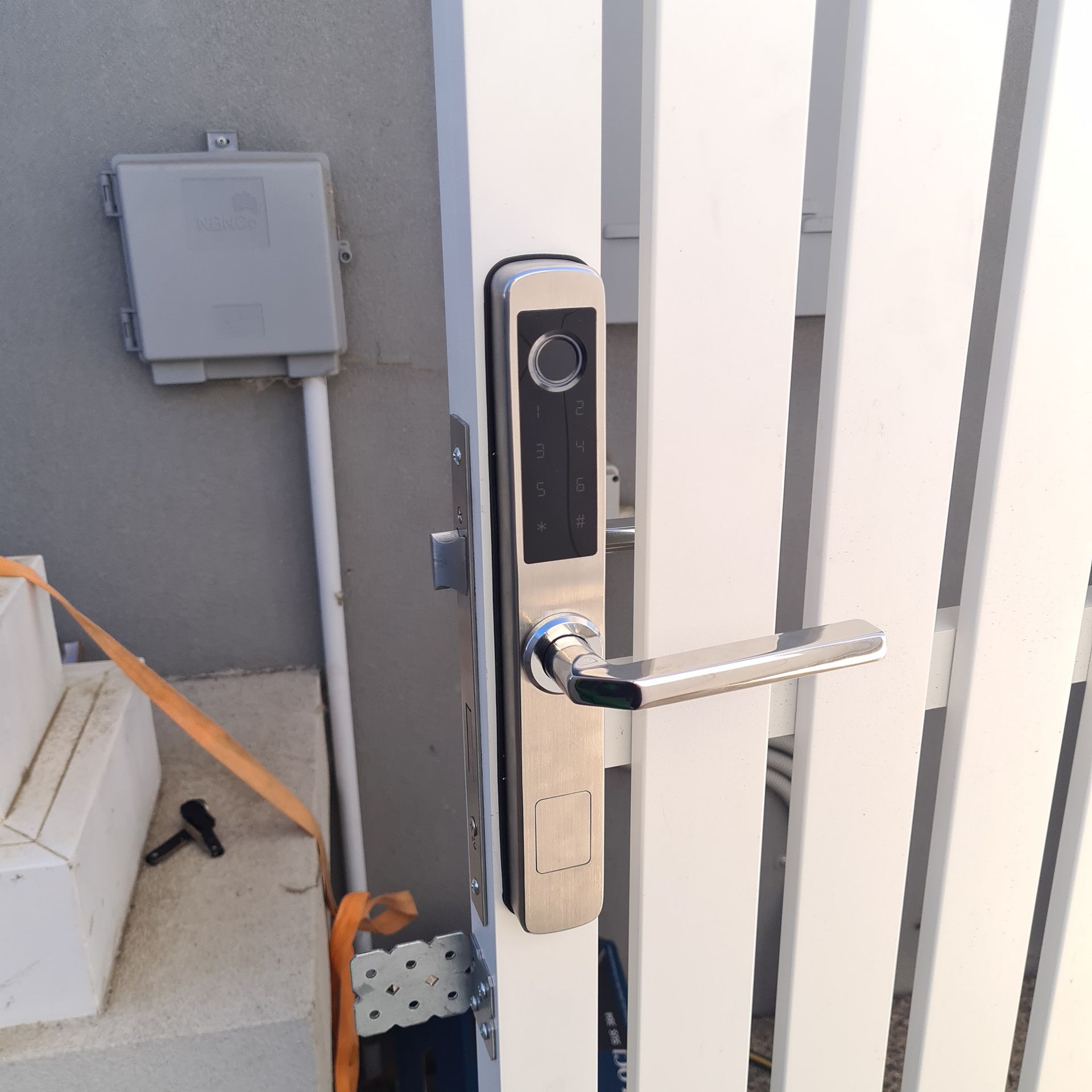A Door With A Stainless Steel Handle Is Behind A White Fence — Barwon Locksmith & Security Doors in Grovedale, VIC