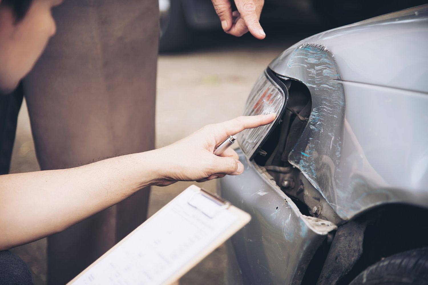 A man is pointing at a damaged car while a woman holds a clipboard.