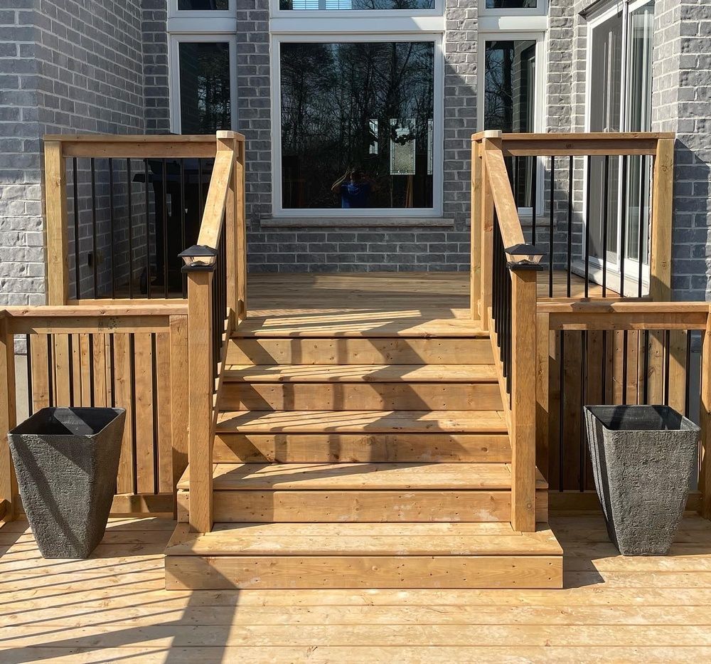 A wooden deck with stairs and planters in front of a brick building