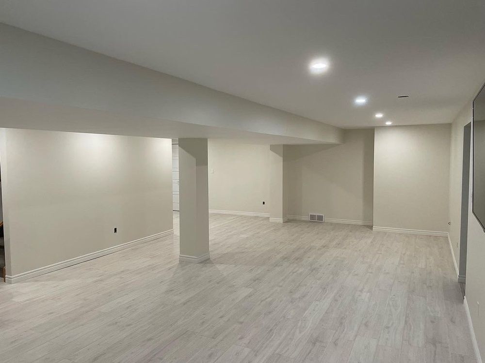 An empty basement with hardwood floors and white walls.