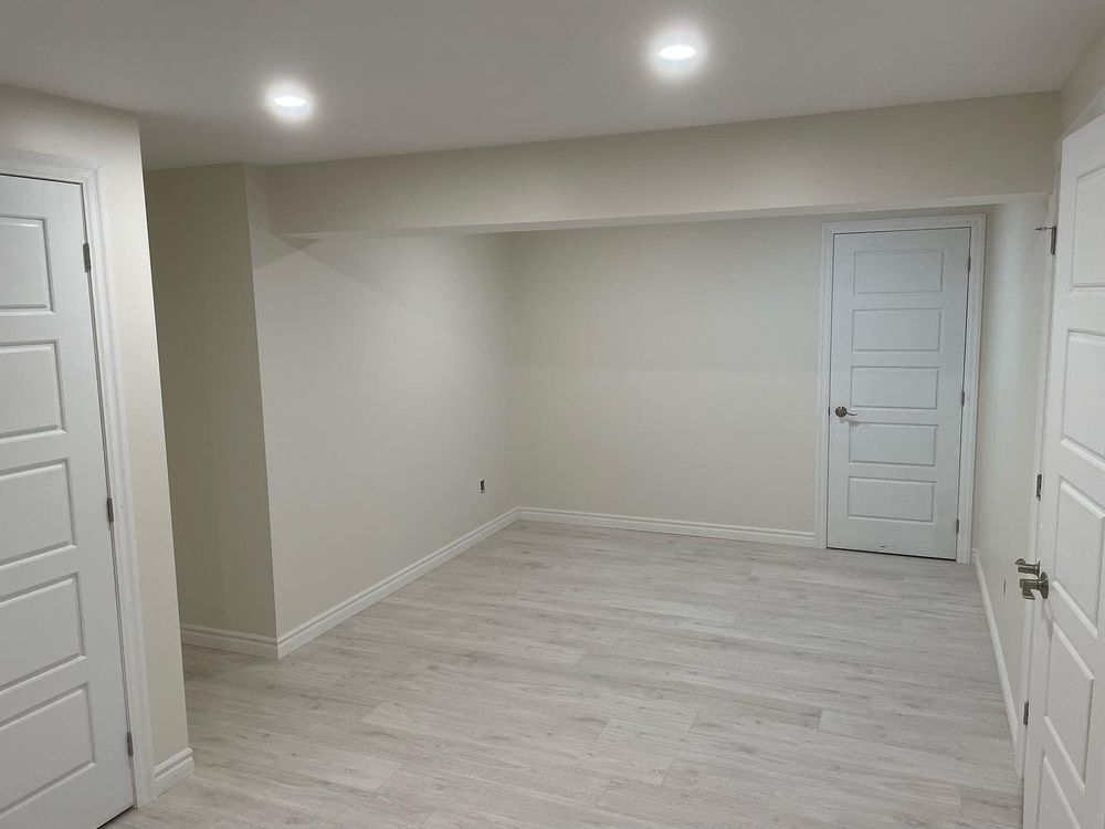 An empty basement with white walls and wooden floors.