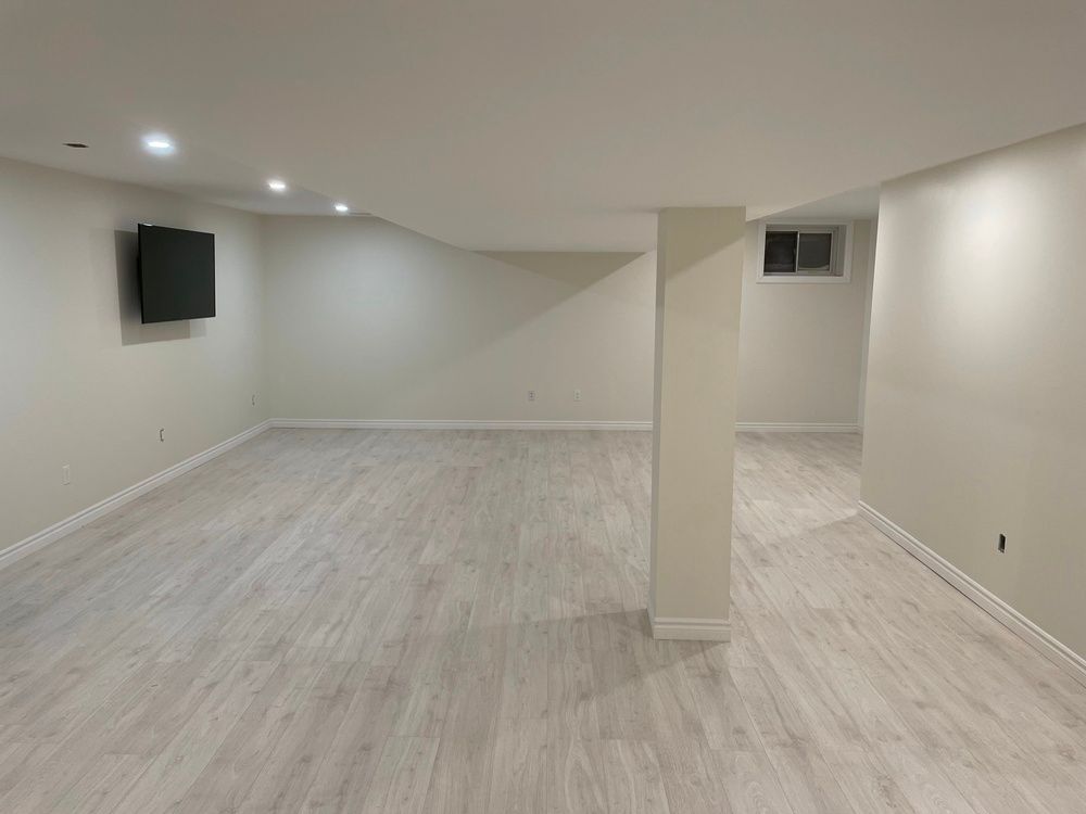 An empty basement with hardwood floors and a flat screen tv mounted on the wall.