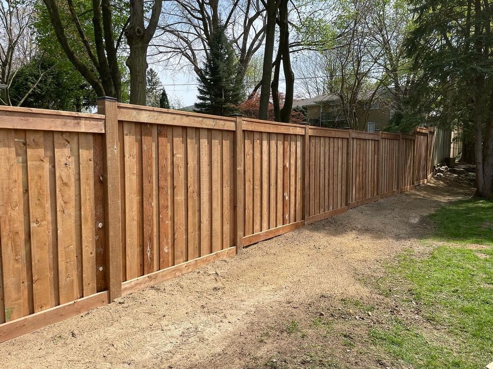 A wooden fence is surrounded by trees and grass in a backyard.