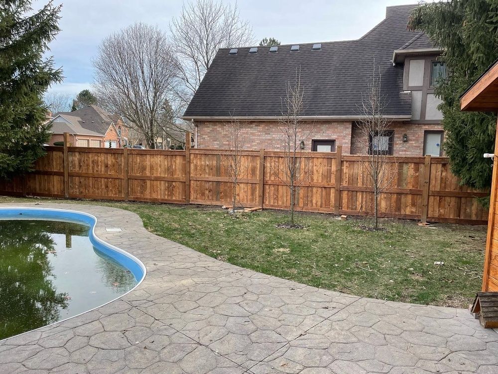 A wooden fence surrounds a swimming pool in a backyard.