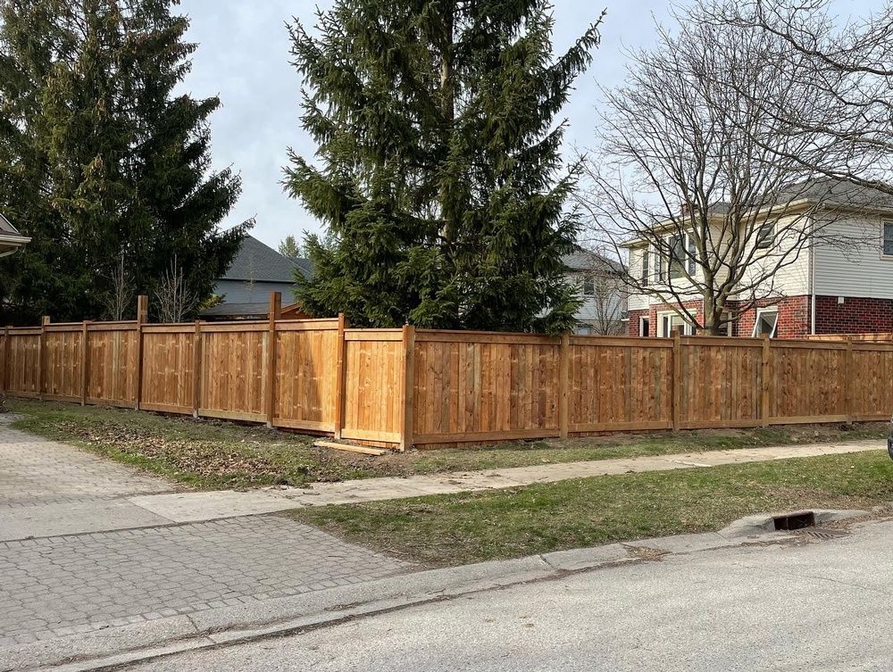 A wooden fence is sitting on the side of the road in front of a house.