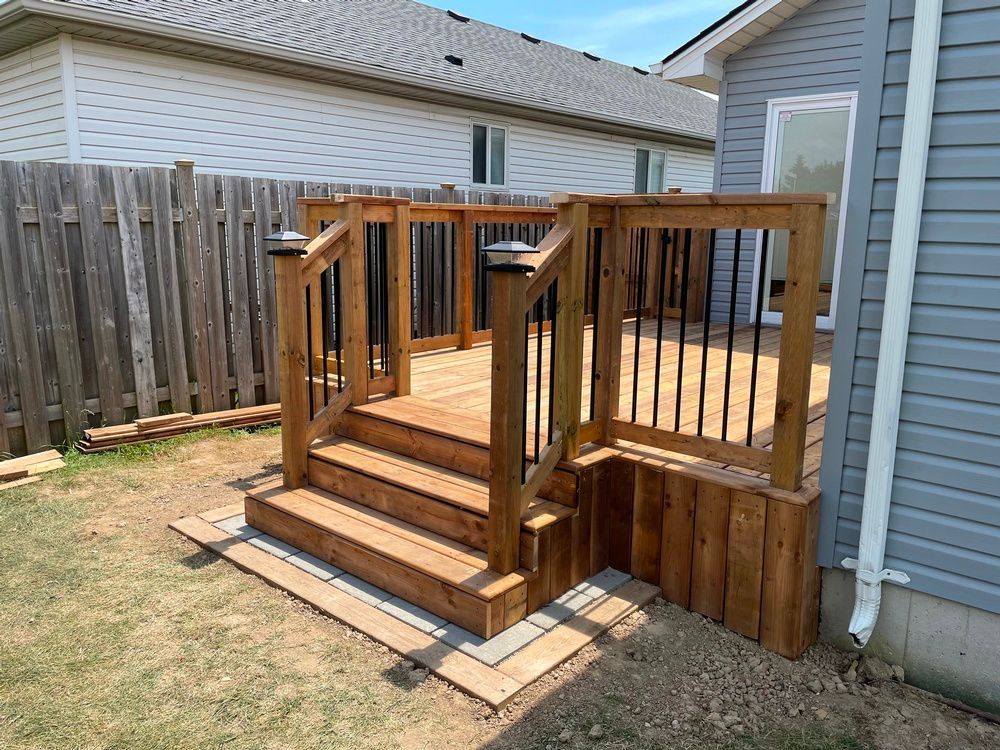 A wooden deck with stairs leading up to it is in the backyard of a house.
