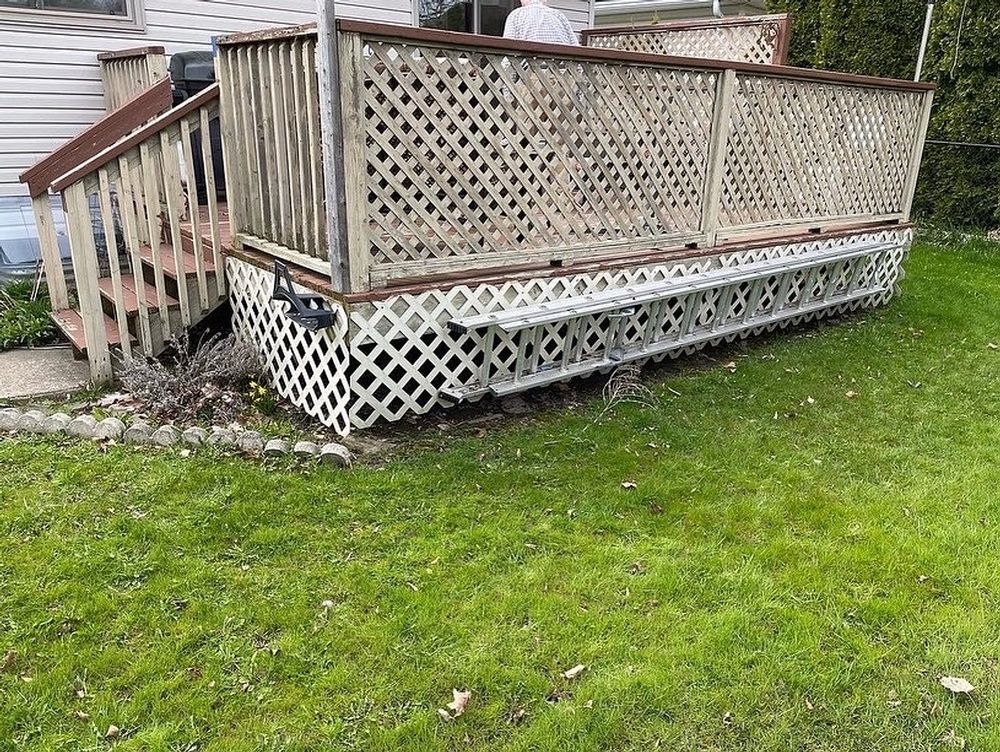 A wooden deck with a ladder attached to it is sitting in the grass in front of a house.