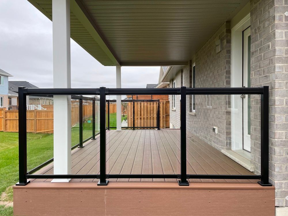 A deck with a glass railing and a brick house in the background.