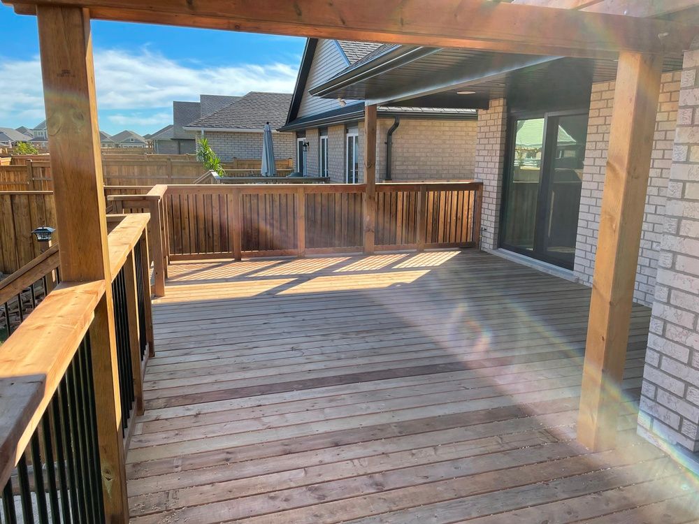 A wooden deck with a pergola and a brick building in the background.